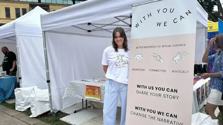 With You We Can organization staff member at community outreach tent displaying sexual violence prevention resources and advocacy materials
