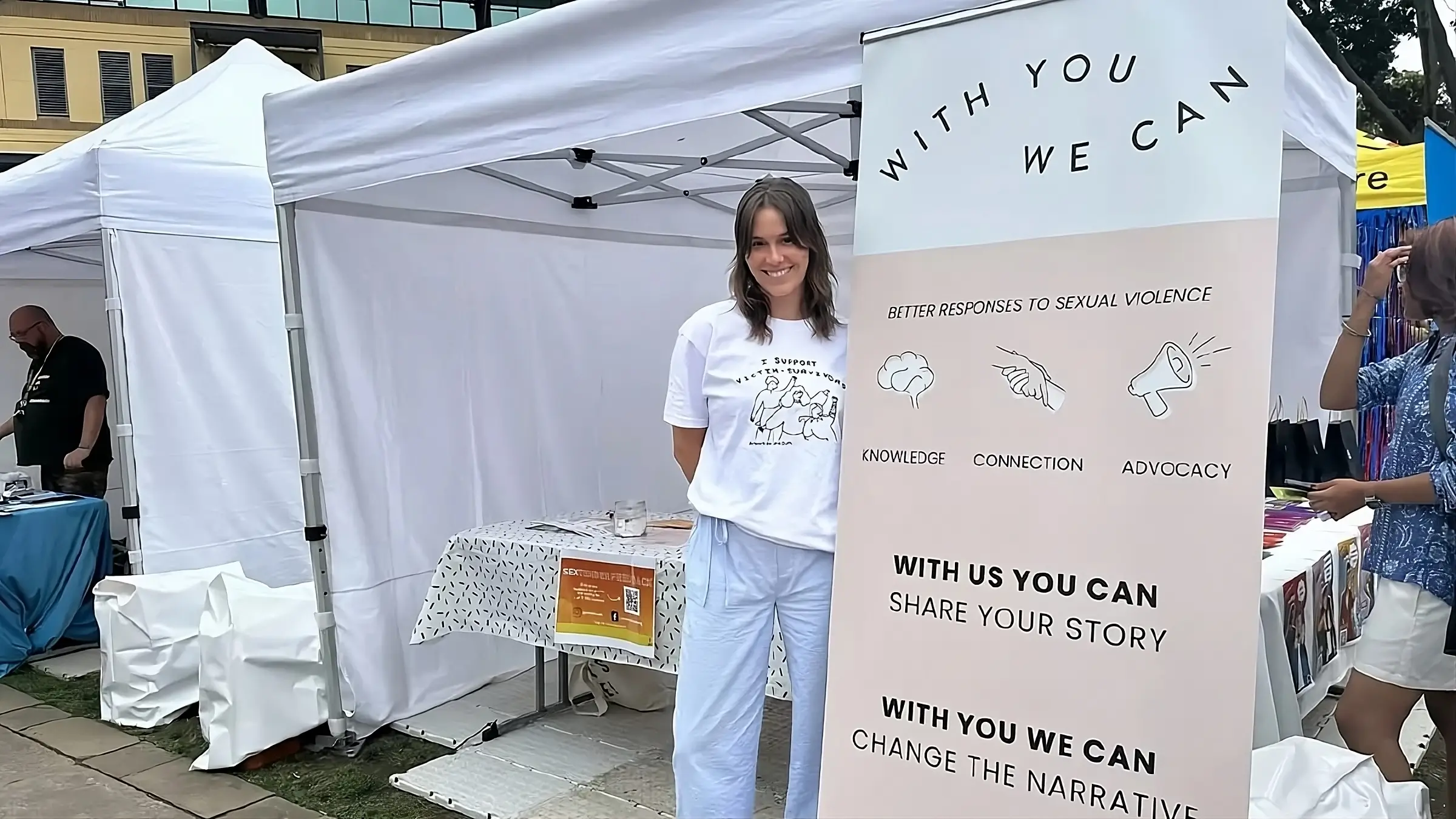 With You We Can organization staff member at community outreach tent displaying sexual violence prevention resources and advocacy materials