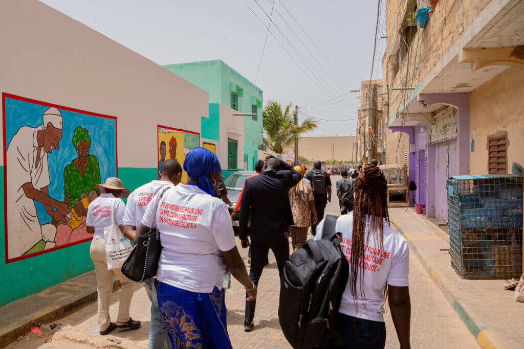 Community health advocates walk through an urban neighbourhood past colourful public health murals.