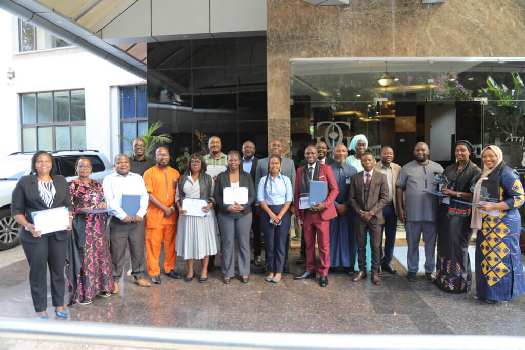 Fellowship participants pose together outside a conference venue, several holding certificates and awards.